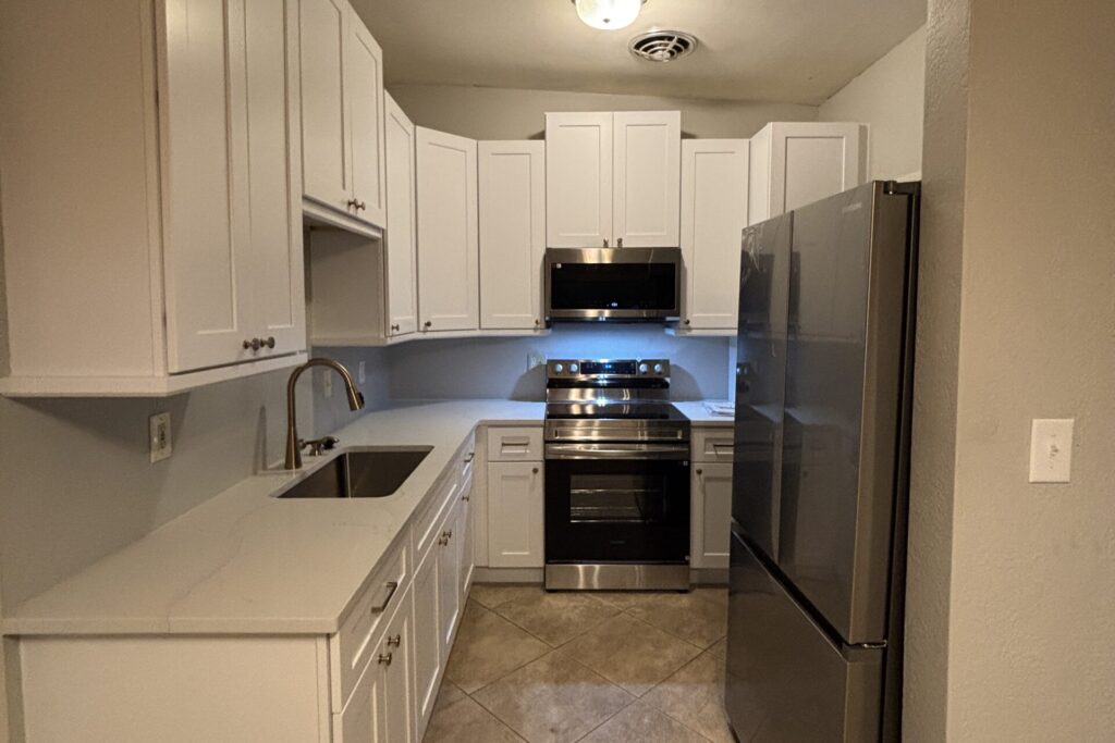 Compact U-shaped kitchen with white shaker cabinets, white countertops, undermount sink, and stainless appliances
