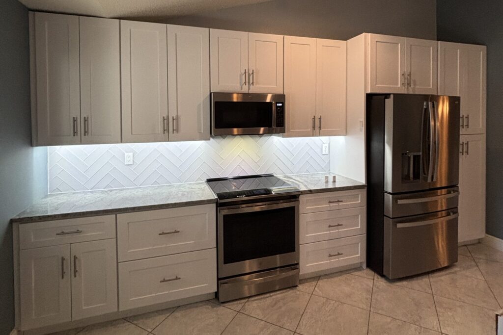 White shaker kitchen with stainless range and refrigerator, white chevron backsplash, and light countertops
