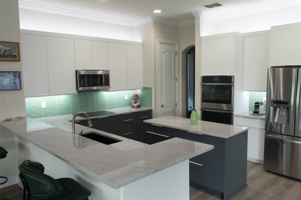 Two-tone kitchen with white upper cabinets, gray lower cabinets, black countertops, glass backsplash, and peninsula sink